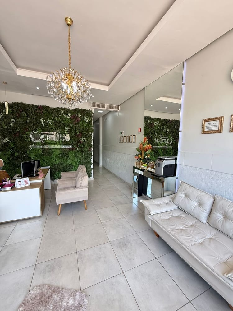 Recepção do Instituto Qualitté com sofá branco, lustre de cristal e parede verde com a logo